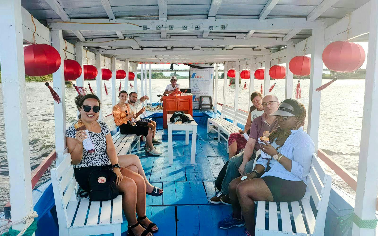 Boat trip to My Son sanctuary with tourists enjoying snacks on a decorated riverboat.