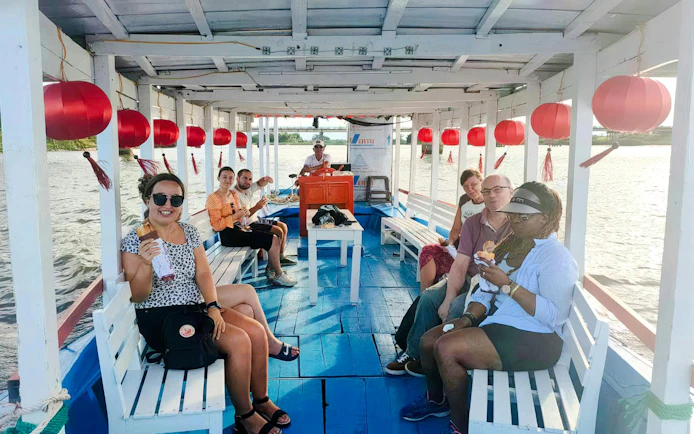 Boat trip to My Son sanctuary with tourists enjoying snacks on a decorated riverboat.