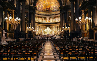 Orchestra Hélios performing in Église de la Madeleine, Paris, with ornate chandeliers and frescoes.