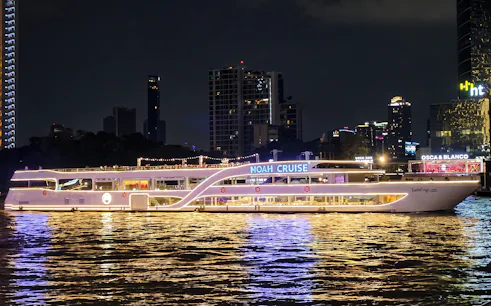 Noah Cruise ship illuminated at night on the Chao Phraya River, Bangkok skyline in background.
