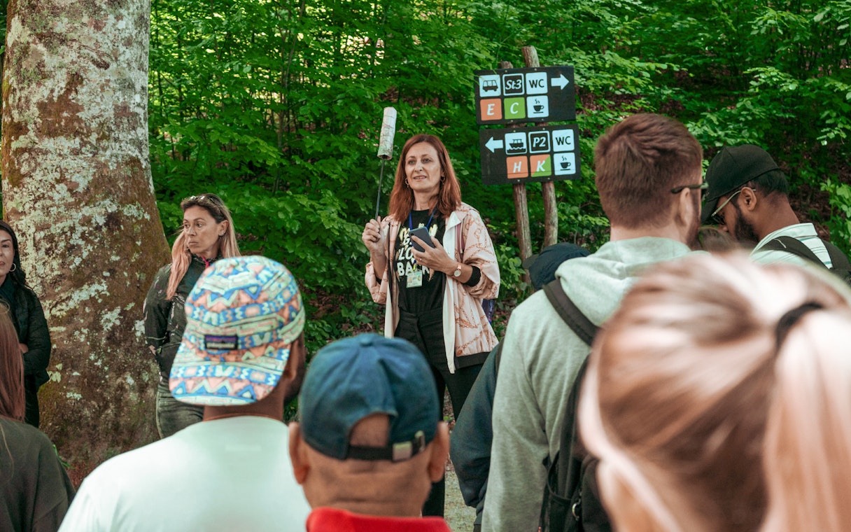 Group listening to a guide in a forested area with directional signs.