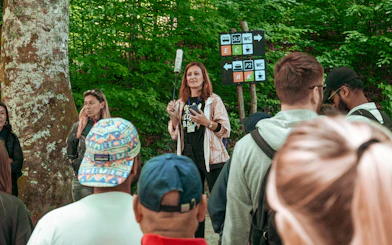 Group listening to a guide in a forested area with directional signs.