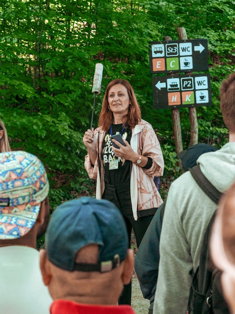 Group listening to a guide in a forested area with directional signs.