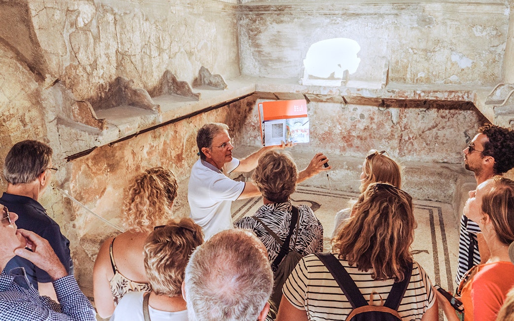 Guide explaining ancient ruins to a group of tourists in Pompeii, Italy.