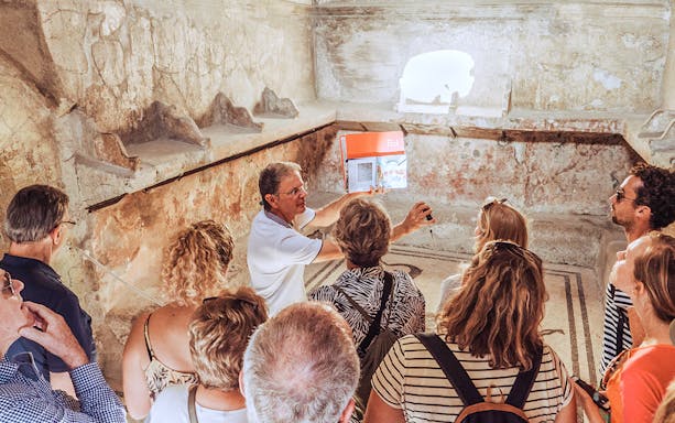 Guide explaining ancient ruins to a group of tourists in Pompeii, Italy.