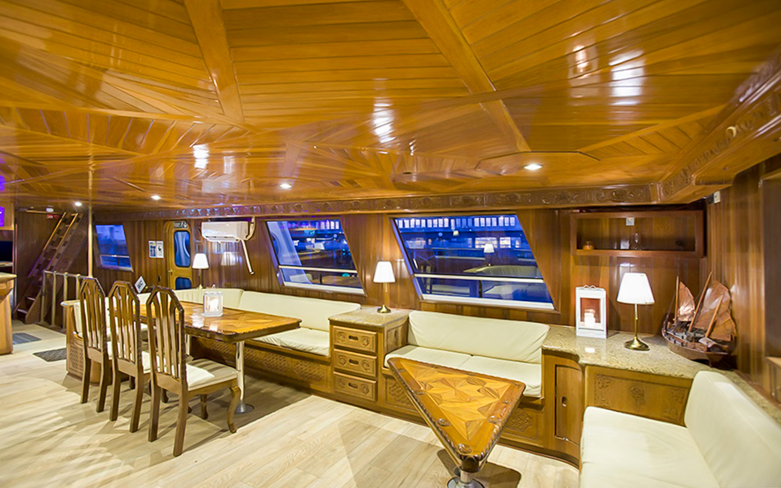 Luxury yacht interior with wooden decor and seating, large windows for whale watching tour.
