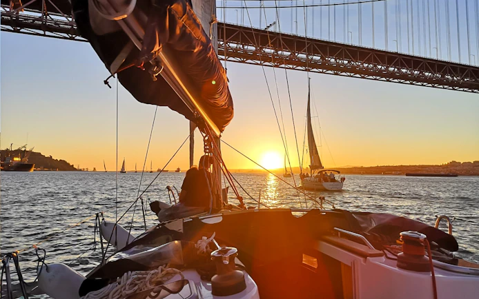 Sailboats on Tagus River at sunset with Lisbon's bridge in view.