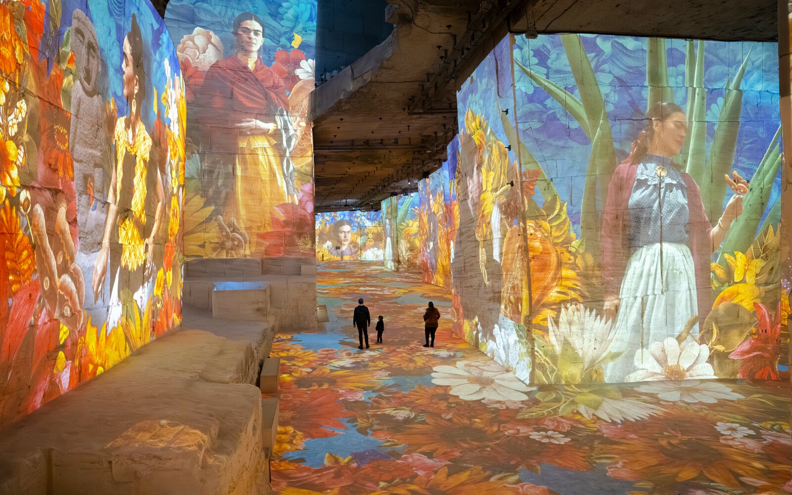 Frida Kahlo artwork projected on walls at Carrières des Lumières exhibit, with visitors walking through.