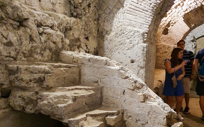 Underground ruins with stone steps and tourists in Naples city tour.