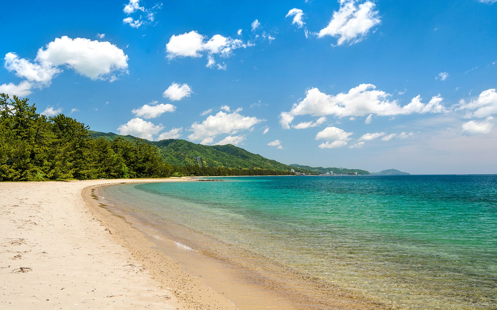 Amanohashidate white sand beach with clear blue water and lush green hills on Kyoto Coastal Tour.