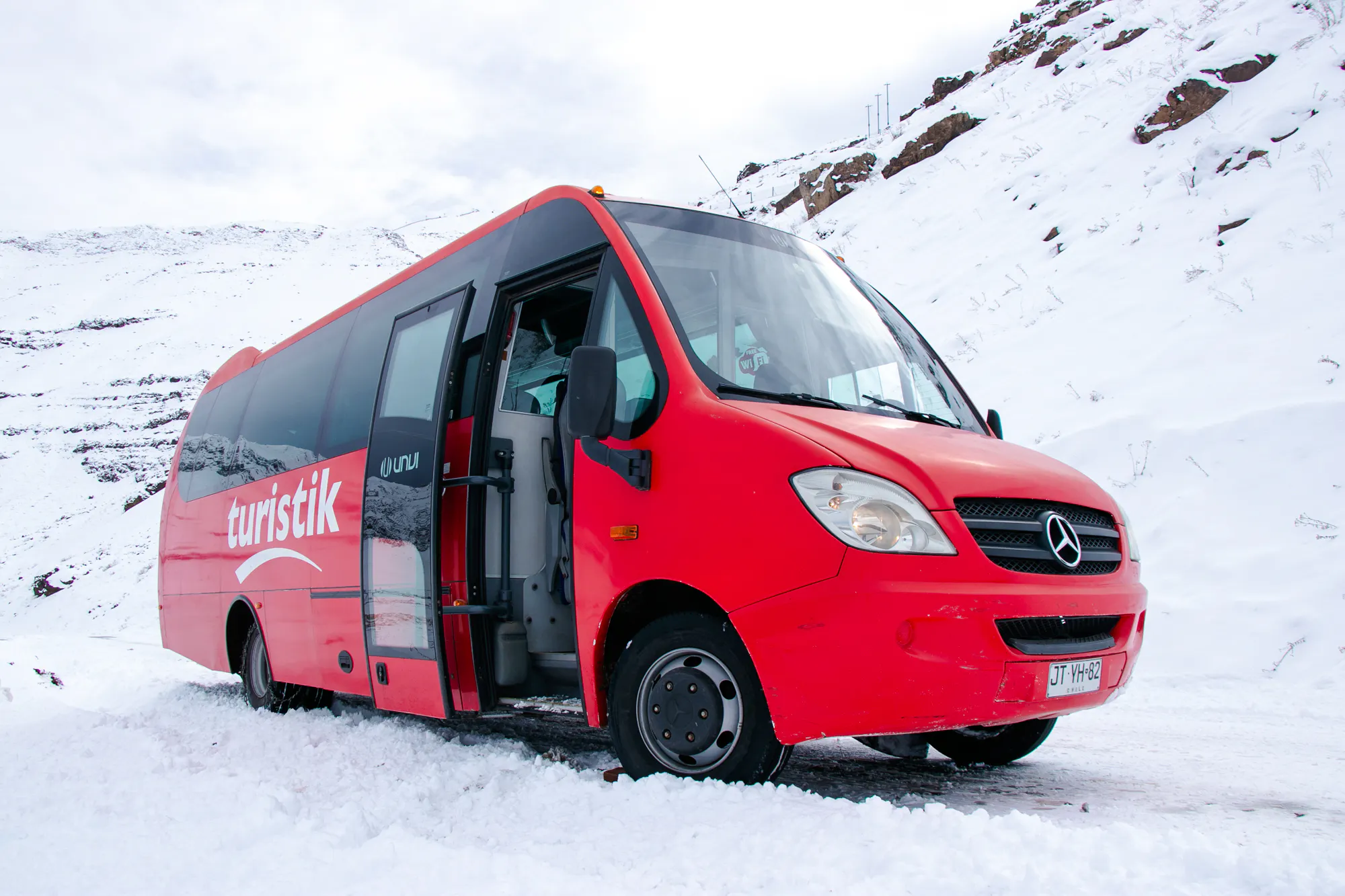 Red tour bus in snowy Valle Nevado, Santiago, ready for excursion.