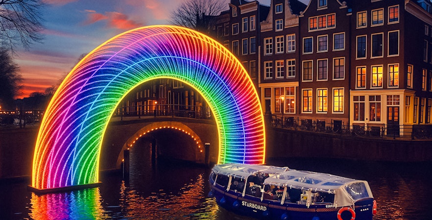 Amsterdam canal cruise passing under illuminated rainbow arch during Light Festival.