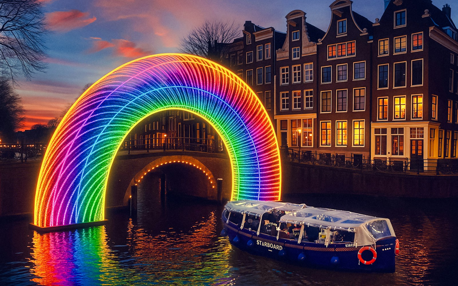 Amsterdam canal cruise passing under illuminated rainbow arch during Light Festival.