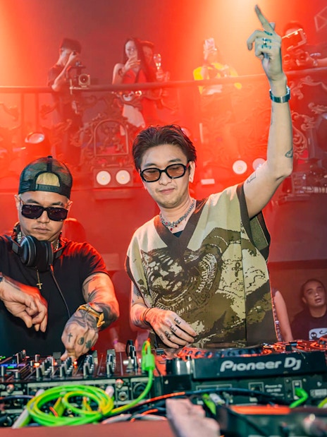 DJs performing at Atlas Super Night Club with vibrant lighting and crowd in the background.