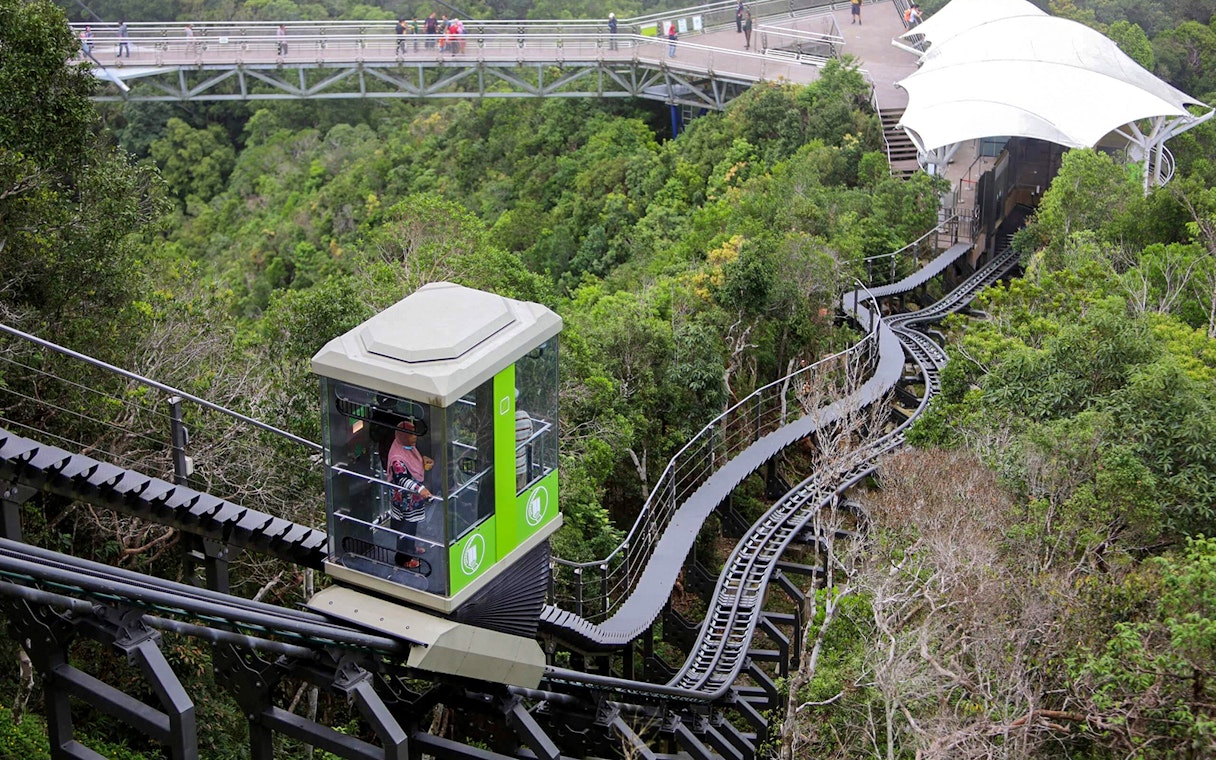 Langkawi SkyGlide ascending through lush forest with SkyBridge in the background.
