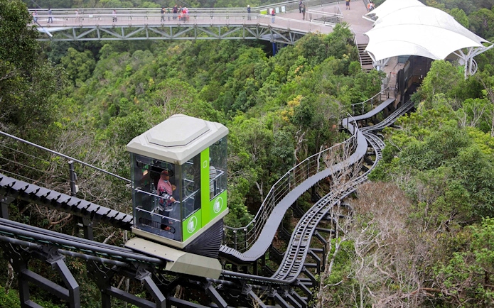 Langkawi SkyGlide ascending through lush forest with SkyBridge in the background.