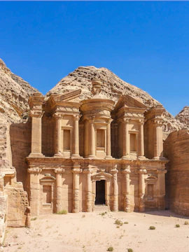 Facade of Ad Deir Monastery in Petra, Jordan, with rocky landscape in background.