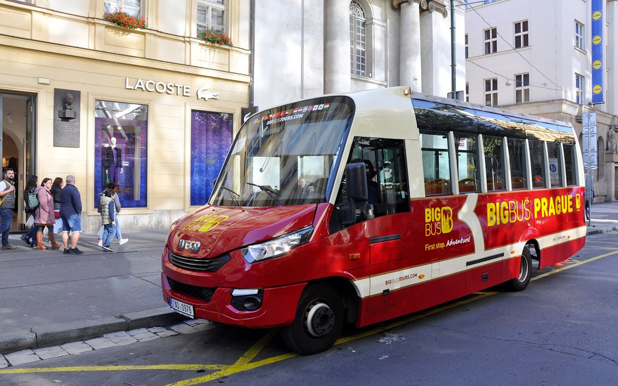 Red Big Bus tour vehicle parked in Prague city center near Lacoste store.
