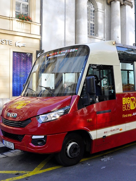 Red Big Bus tour vehicle parked in Prague city center near Lacoste store.