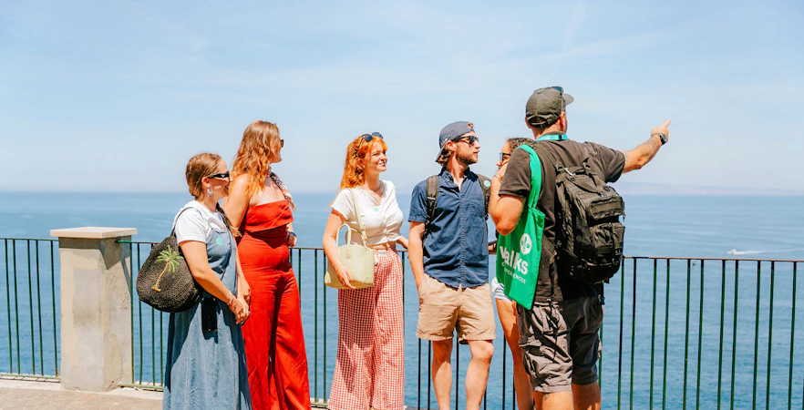Tour group enjoying Amalfi Coast views with guide pointing at the sea.