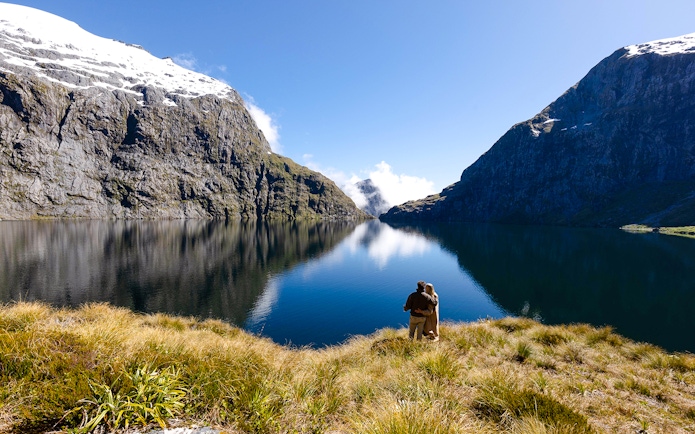 Couple overlooking Lake Quill during helicopter ride from Milford Sound, surrounded by fjord cliffs.