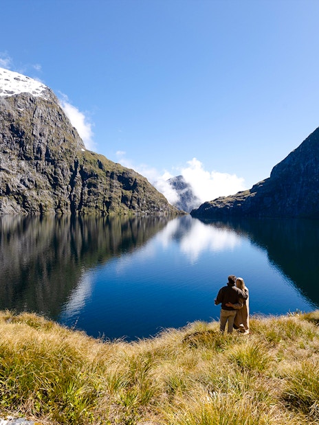 Couple overlooking Lake Quill during helicopter ride from Milford Sound, surrounded by fjord cliffs.