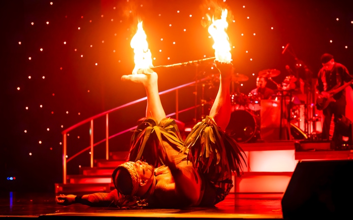 Fire dancer performing with flaming sticks on stage at Rock-A-Hula show.