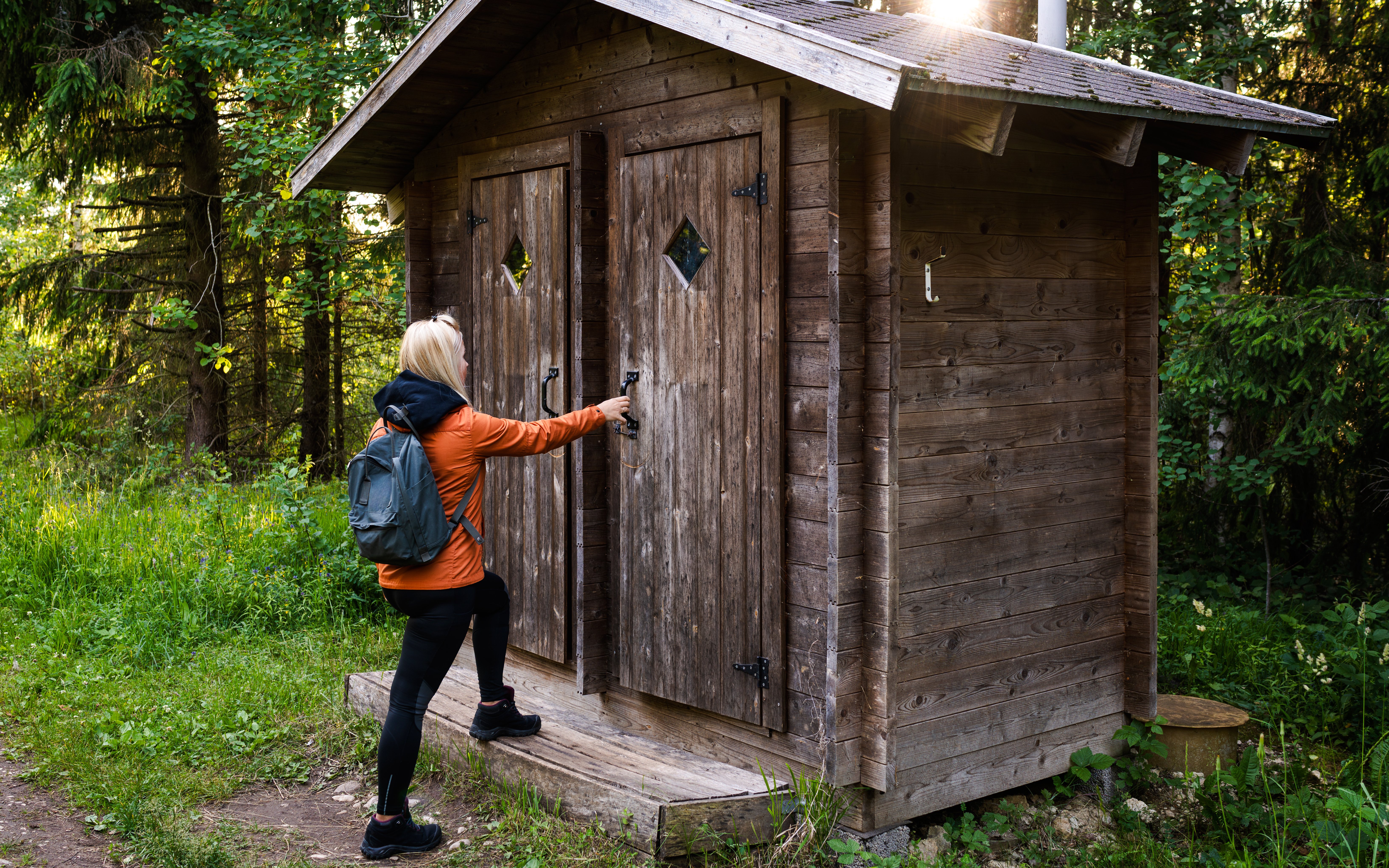 Hiker opening a wooden toilet door on a forest trail.