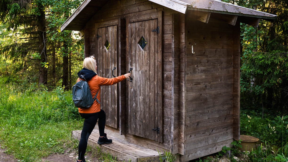 Hiker opening a wooden toilet door on a forest trail.