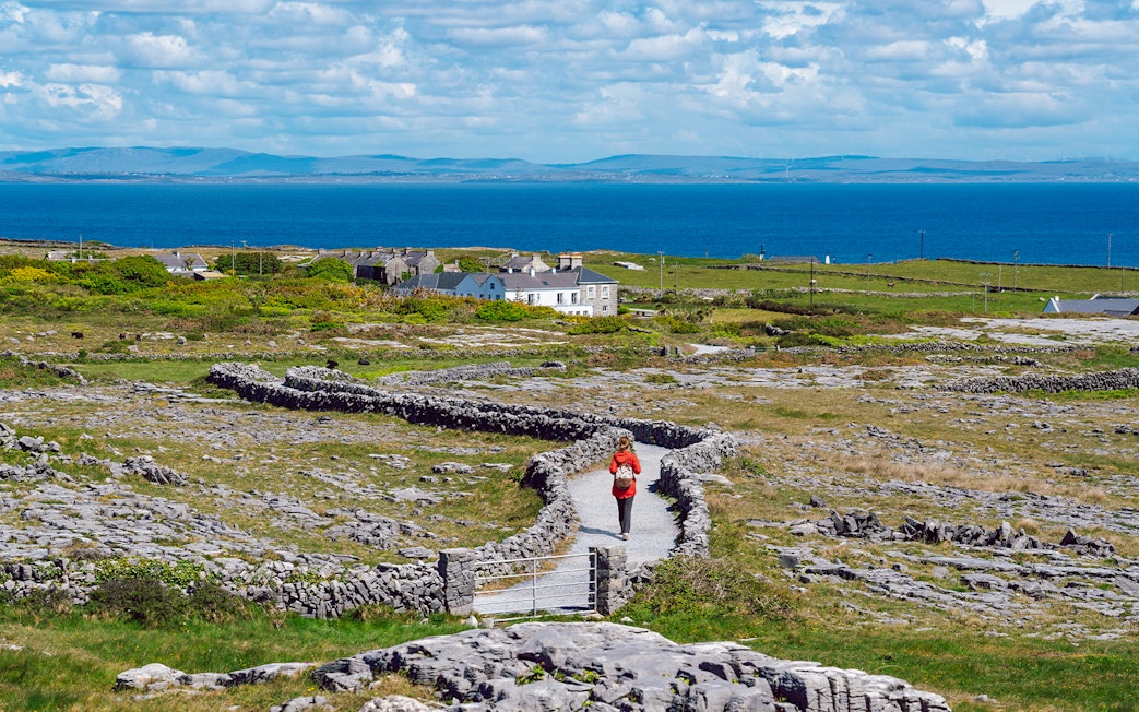 Tourist walking a stone path on Inishmore, Aran Islands, with ocean view.