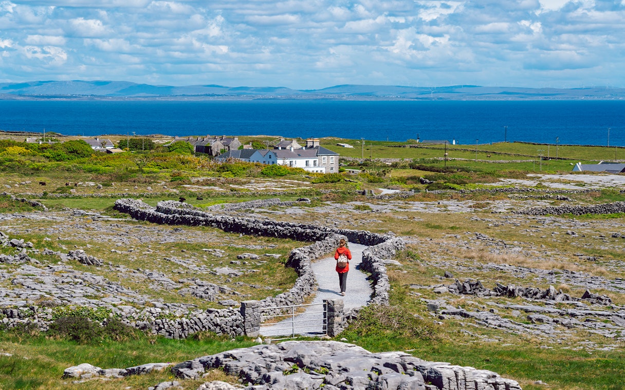 Tourist walking a stone path on Inishmore, Aran Islands, with ocean view.