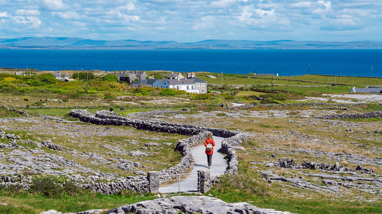 Tourist walking a stone path on Inishmore, Aran Islands, with ocean view.