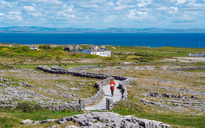 Tourist walking a stone path on Inishmore, Aran Islands, with ocean view.