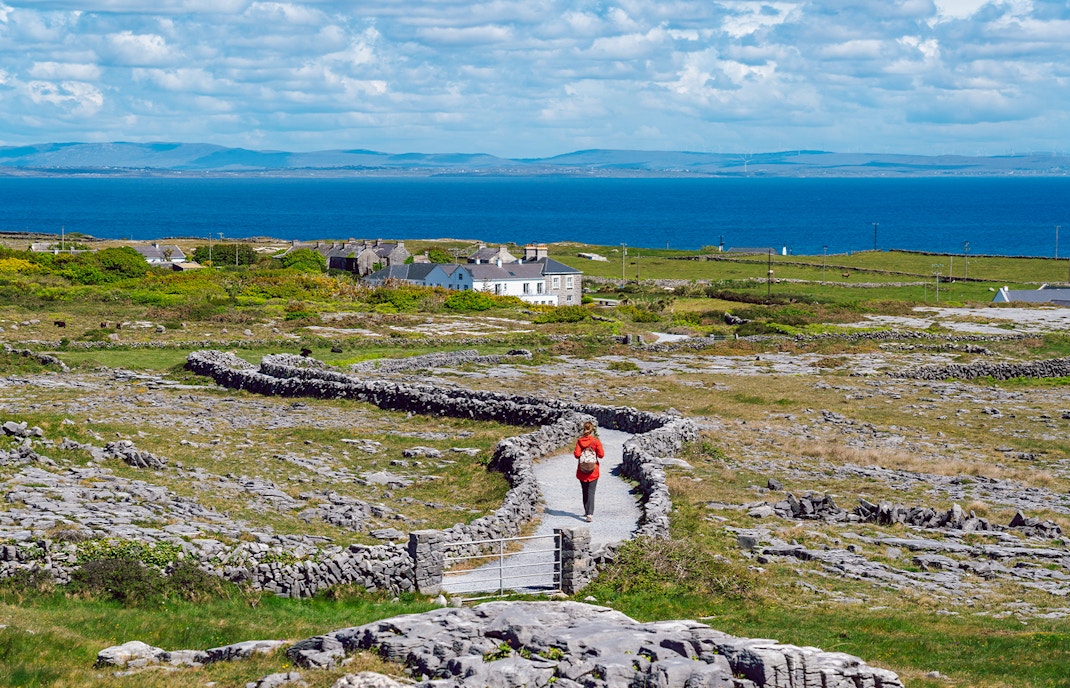 Tourist walking a stone path on Inishmore, Aran Islands, with ocean view.
