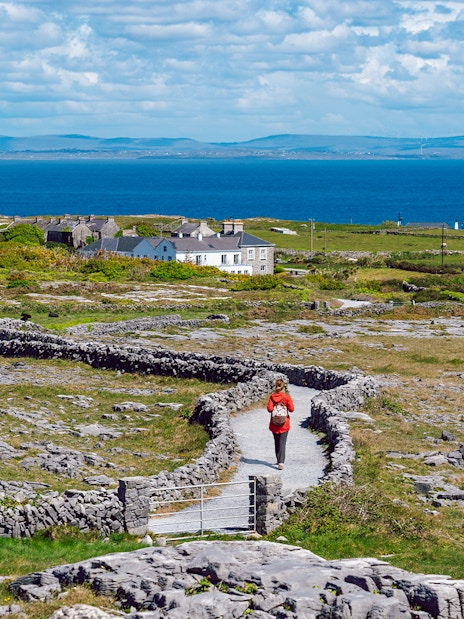 Tourist walking a stone path on Inishmore, Aran Islands, with ocean view.