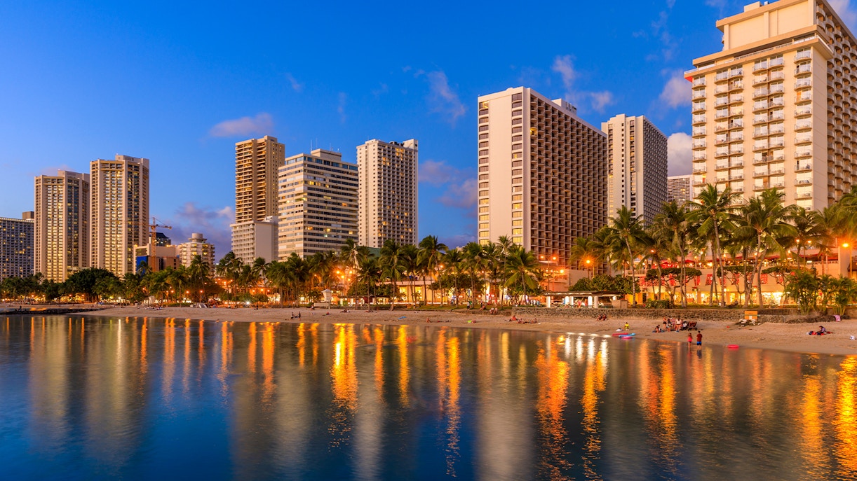 Waikiki Beach at sunset with city skyline reflections in Honolulu, Oahu, Hawaii.