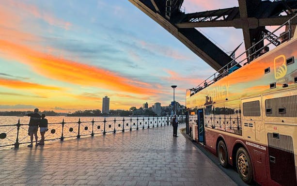 Big bus parked near Sydney Harbour at sunset.