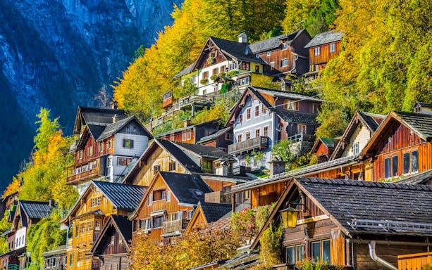Wooden houses on a hillside in Hallstatt's old town, Austria, surrounded by autumn foliage.