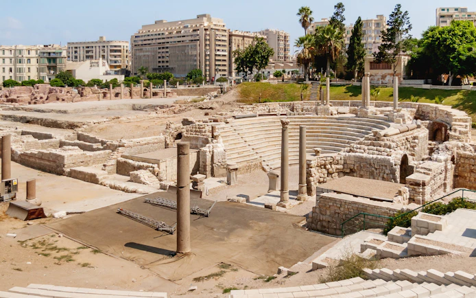 Ruins of the Roman amphitheatre in Alexandria, Egypt, with stone seating and columns.
