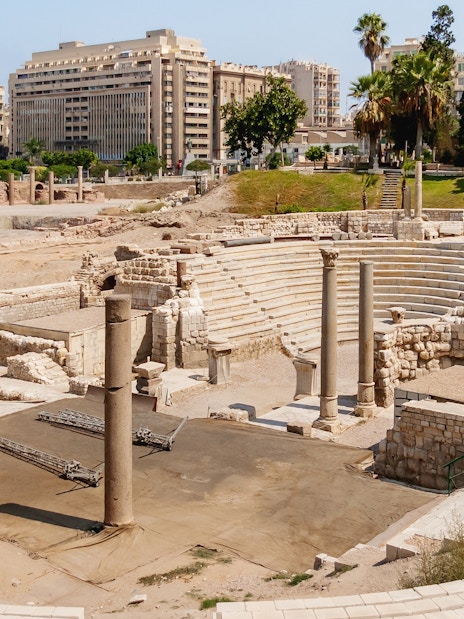 Ruins of the Roman amphitheatre in Alexandria, Egypt, with stone seating and columns.