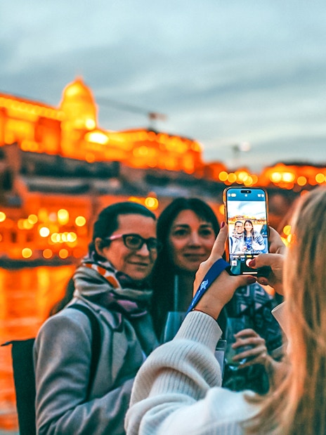 Guests taking photos on a New Year's Eve dinner cruise with illuminated cityscape in the background.