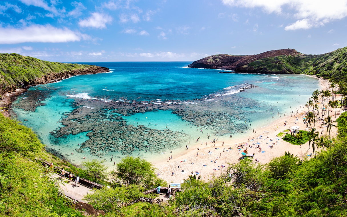 Hanauma Bay, Oahu with visitors snorkeling in clear blue waters and relaxing on the sandy beach.