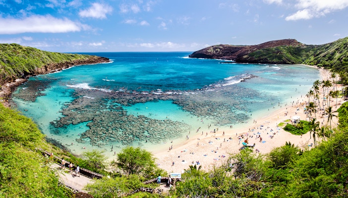 Hanauma Bay, Oahu with visitors snorkeling in clear blue waters and relaxing on the sandy beach.