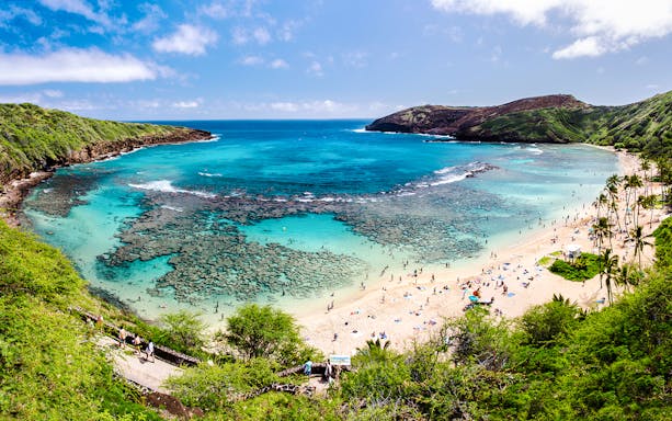 Hanauma Bay, Oahu with visitors snorkeling in clear blue waters and relaxing on the sandy beach.