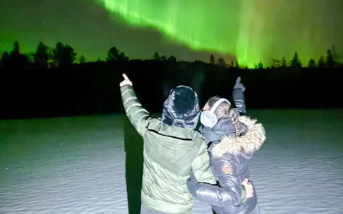 Guests pointing at Northern Lights during tour in Rovaniemi.