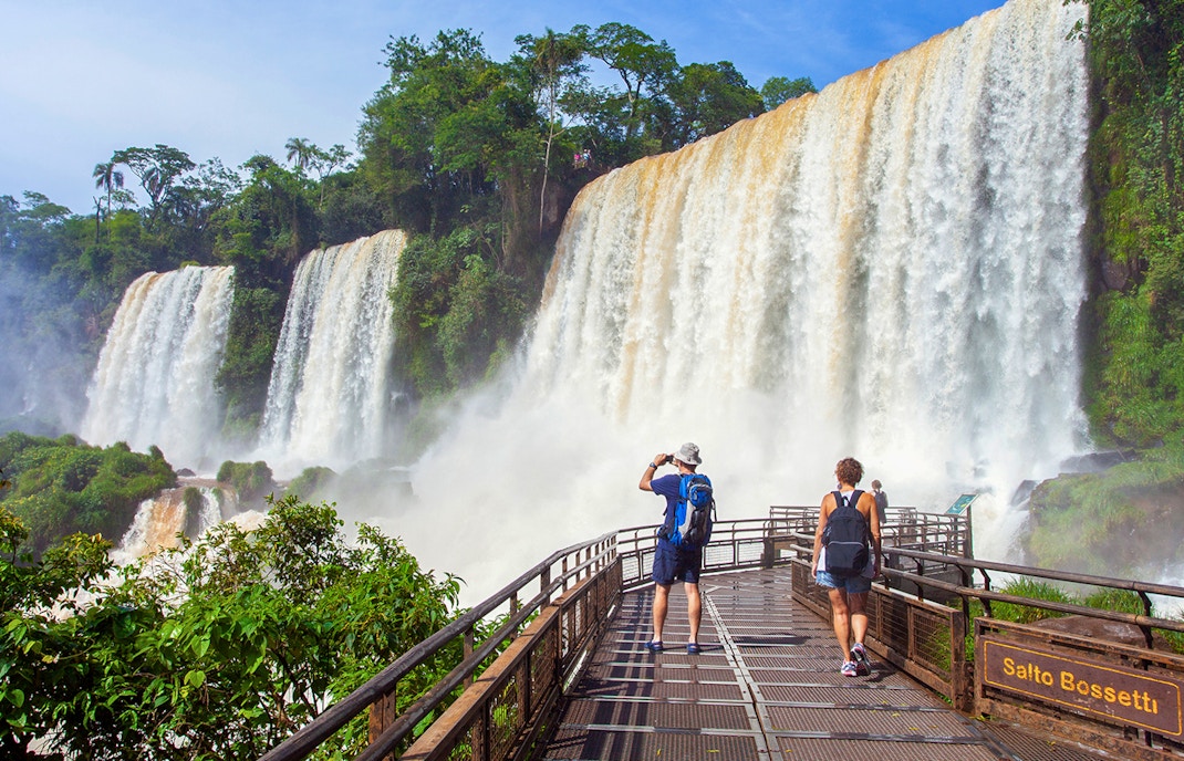 Tourists viewing the cascading Iguazu Falls from a wooden platform in Argentina.