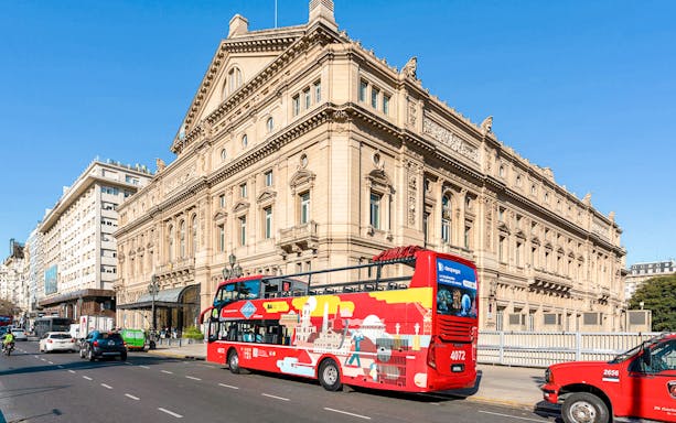 Hop on Hop off city bus in front of Teatro Colón, Buenos Aires, with tourists exploring the historic landmark.