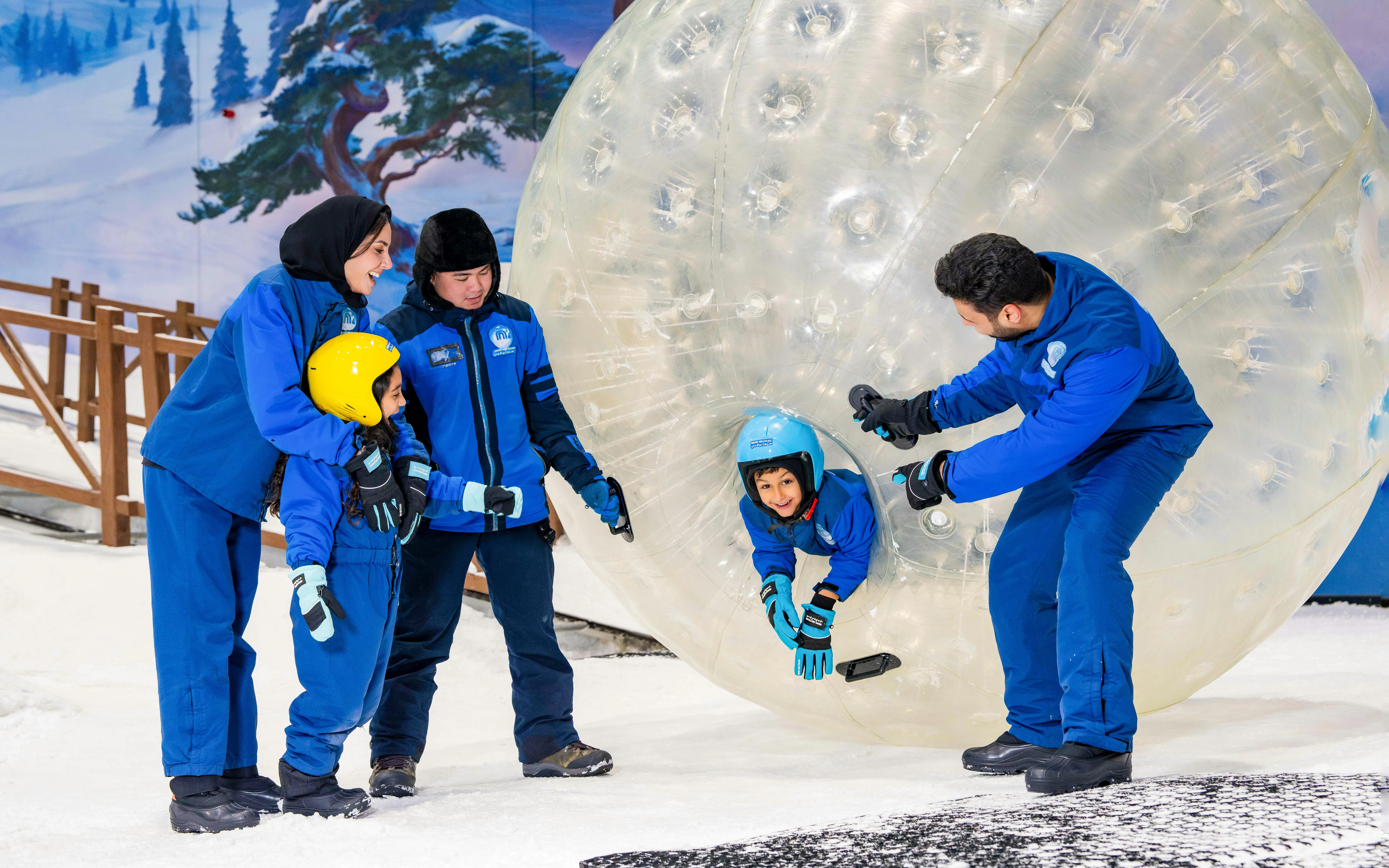 Child entering Zorb ball on snow with guides in Abu Dhabi.