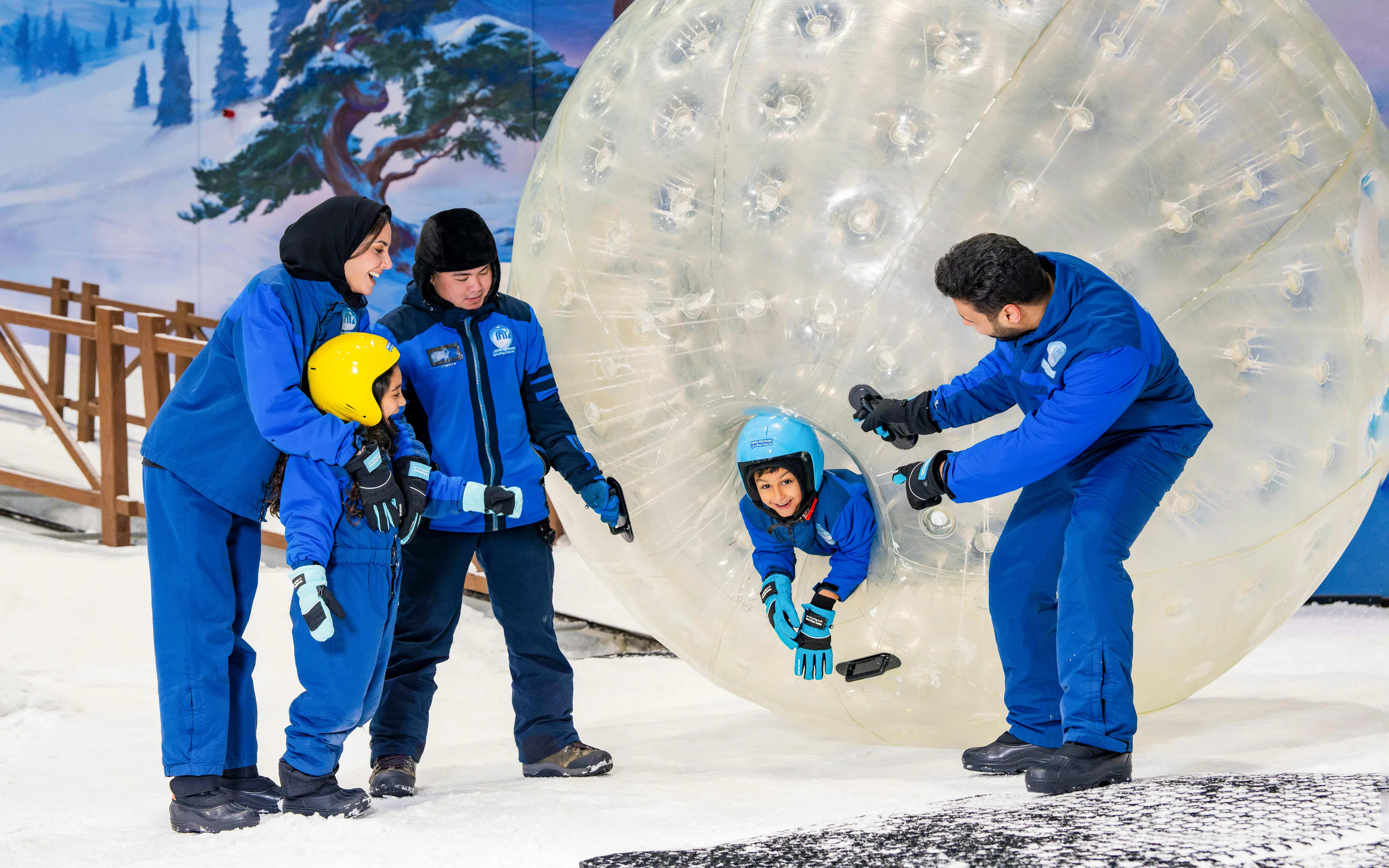 Child entering Zorb ball on snow with guides in Abu Dhabi.