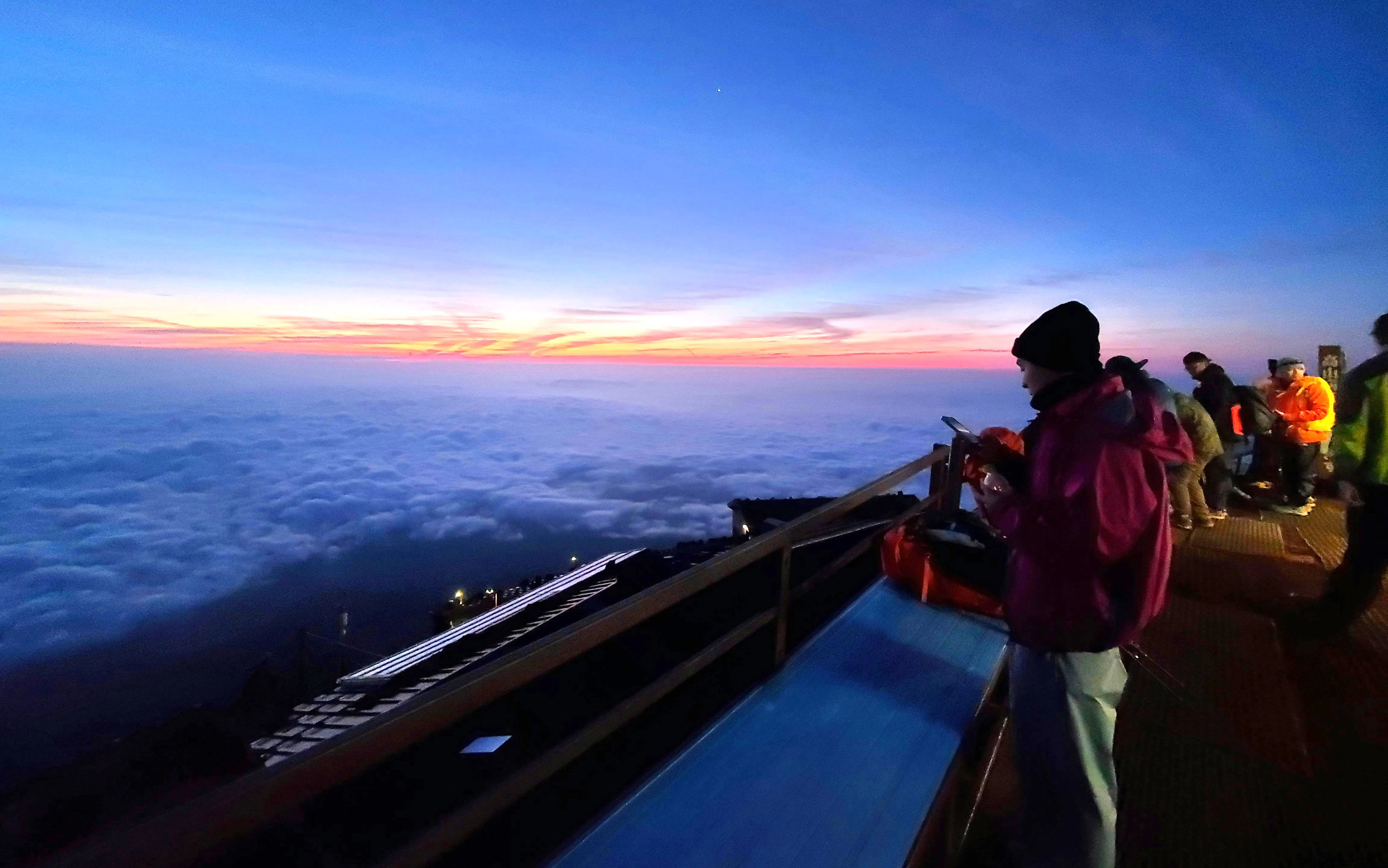 Climbers watching sunrise above clouds on Mt. Fuji summit during climbing tour.